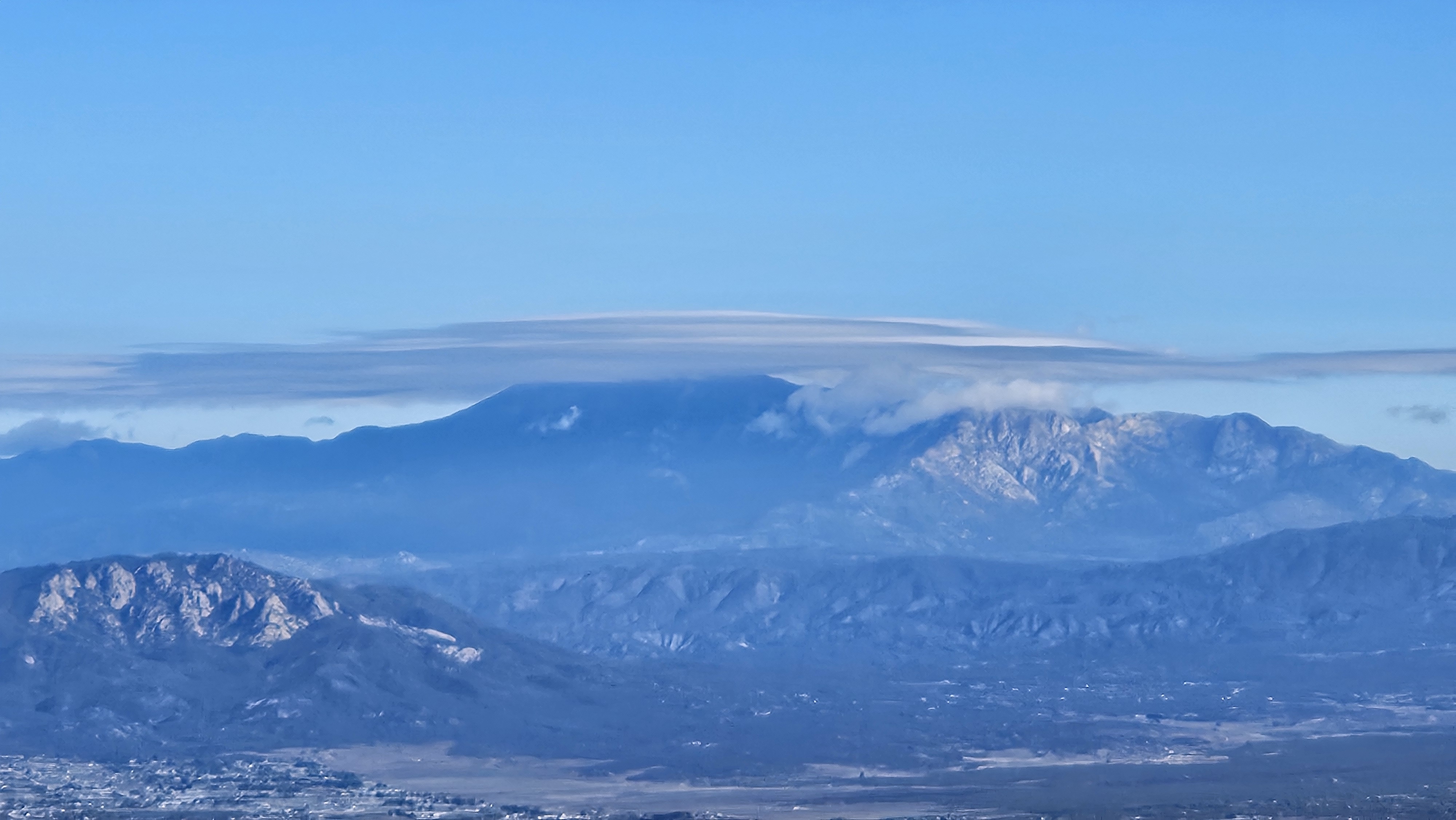 A high peak on the horizon capped by a single smooth lenticular cloud