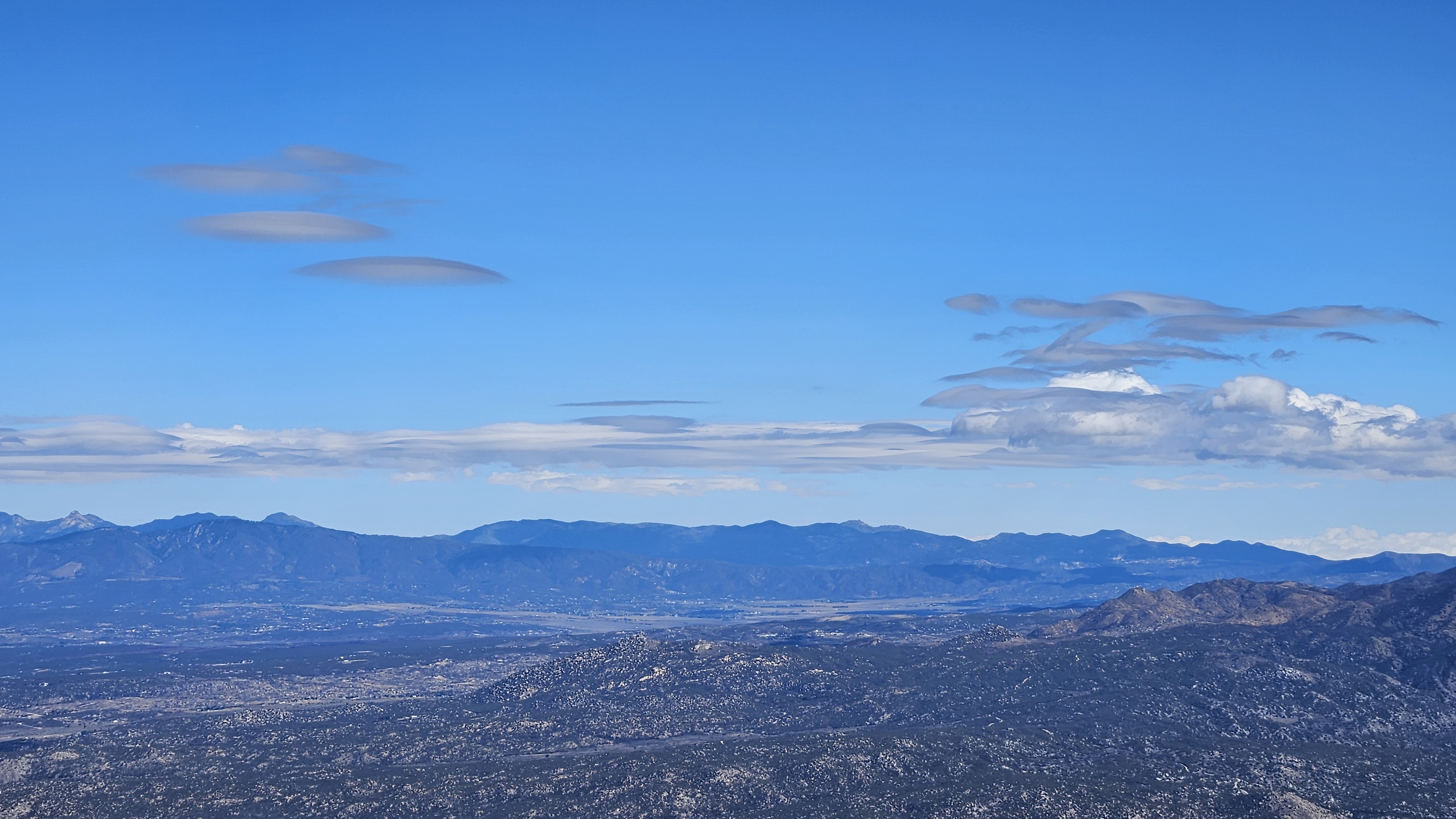 A lenticular cloud breaking up and spreading just east of a distant high peak